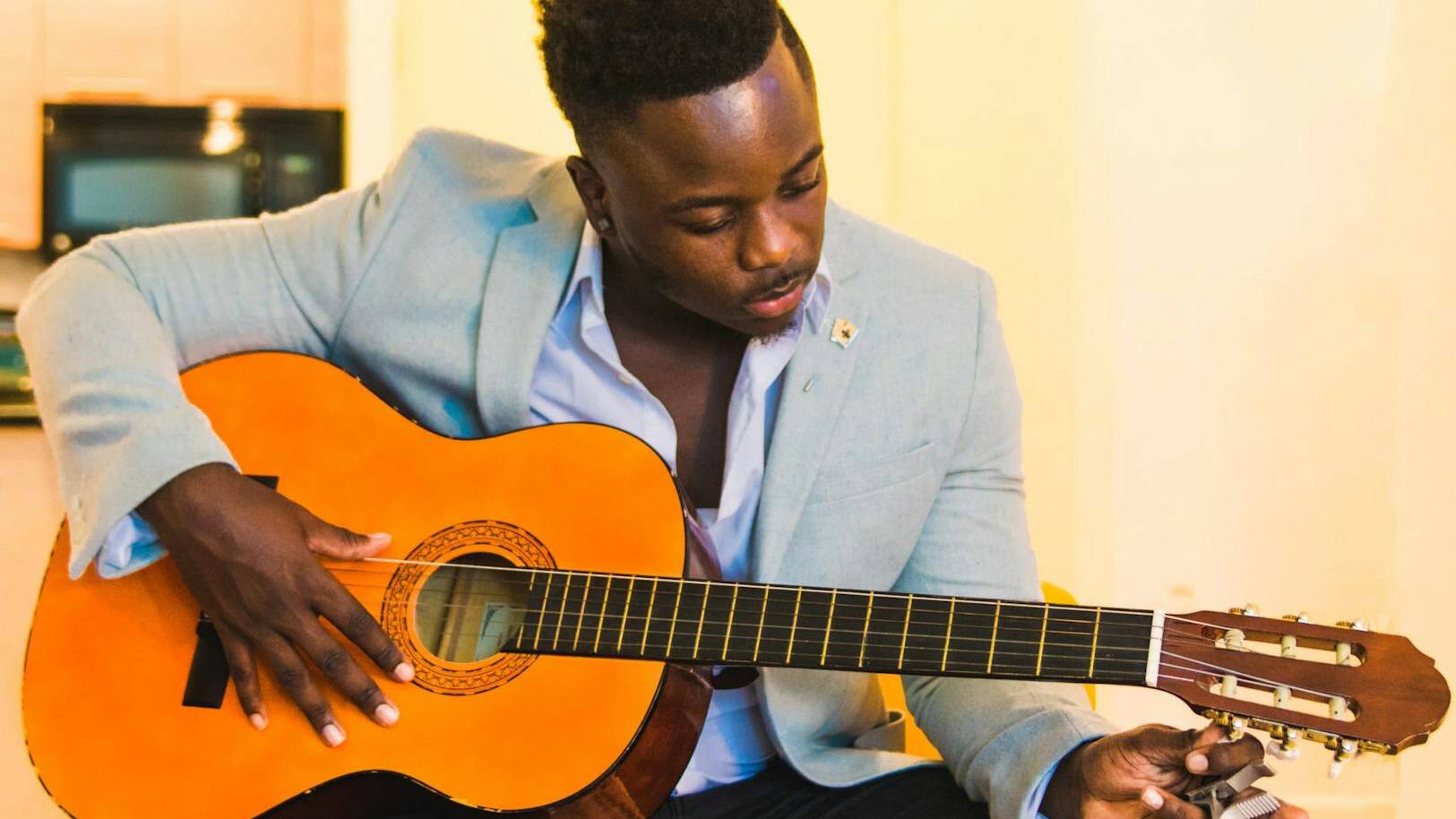 man wearing blue coat and black distressed bottoms holding brown classical guitar